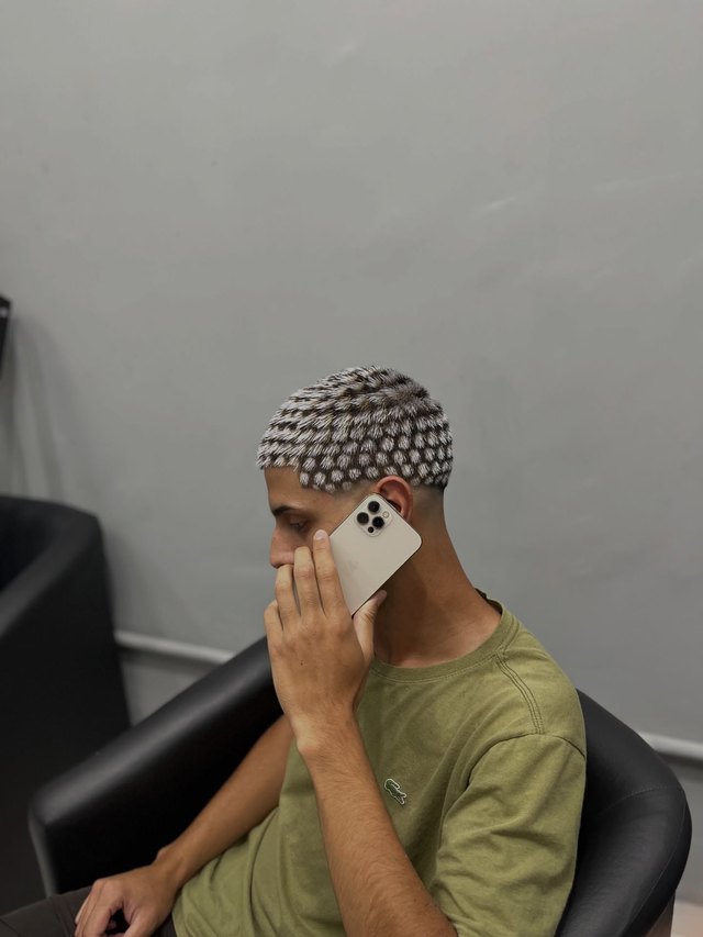 Cliente com o cabelo descolorido em desenho de pontos, falando ao telefone na cadeira.