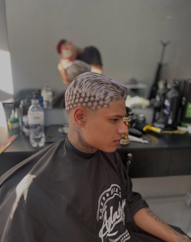 Desenho de pontos descoloridos no topo da cabeça, cliente de capa preta da barbearia.