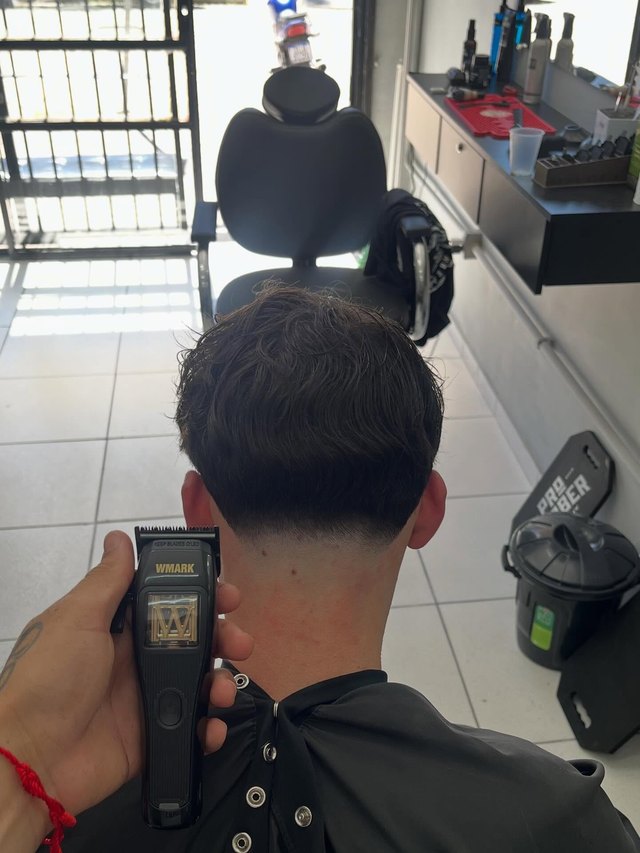 Máquina passando na nuca, acabamento visto por trás dentro da barbearia.