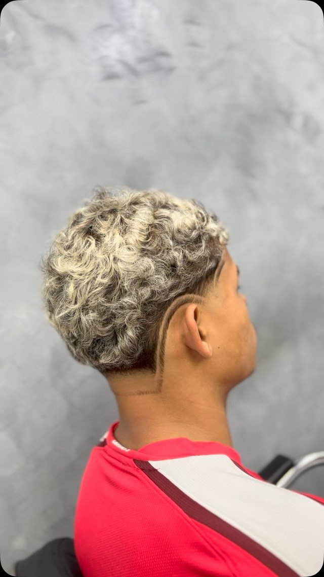 Cabelo cacheado com luzes claras, visto de trás contra a parede de concreto.