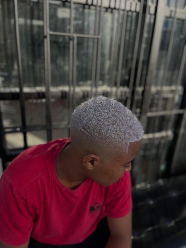 Cabelo platinado num degradê curto, cliente de camiseta vermelha.